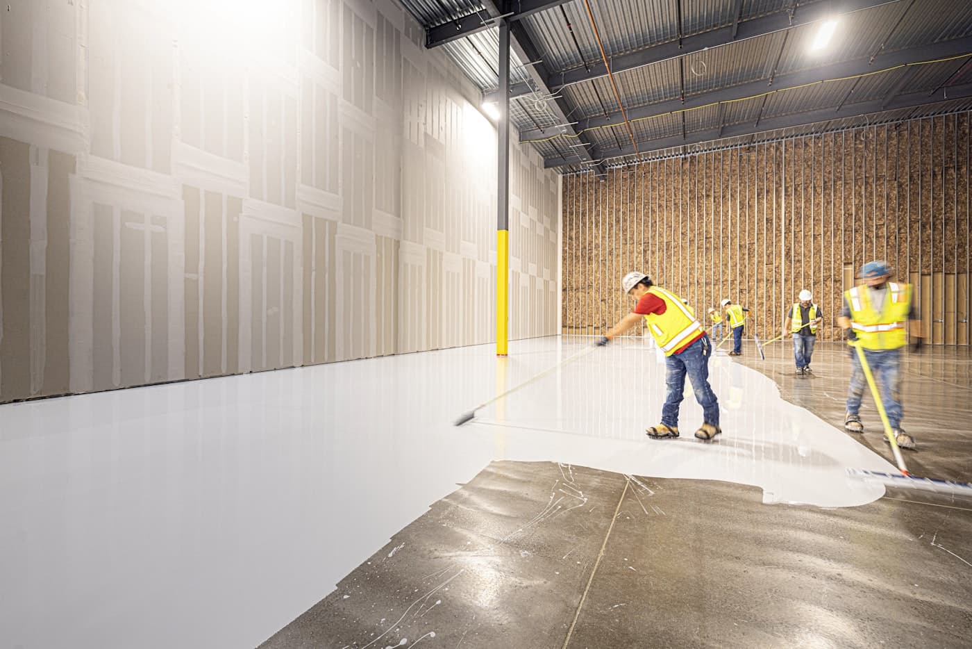 Crew applying epoxy coating across a large industrial floor