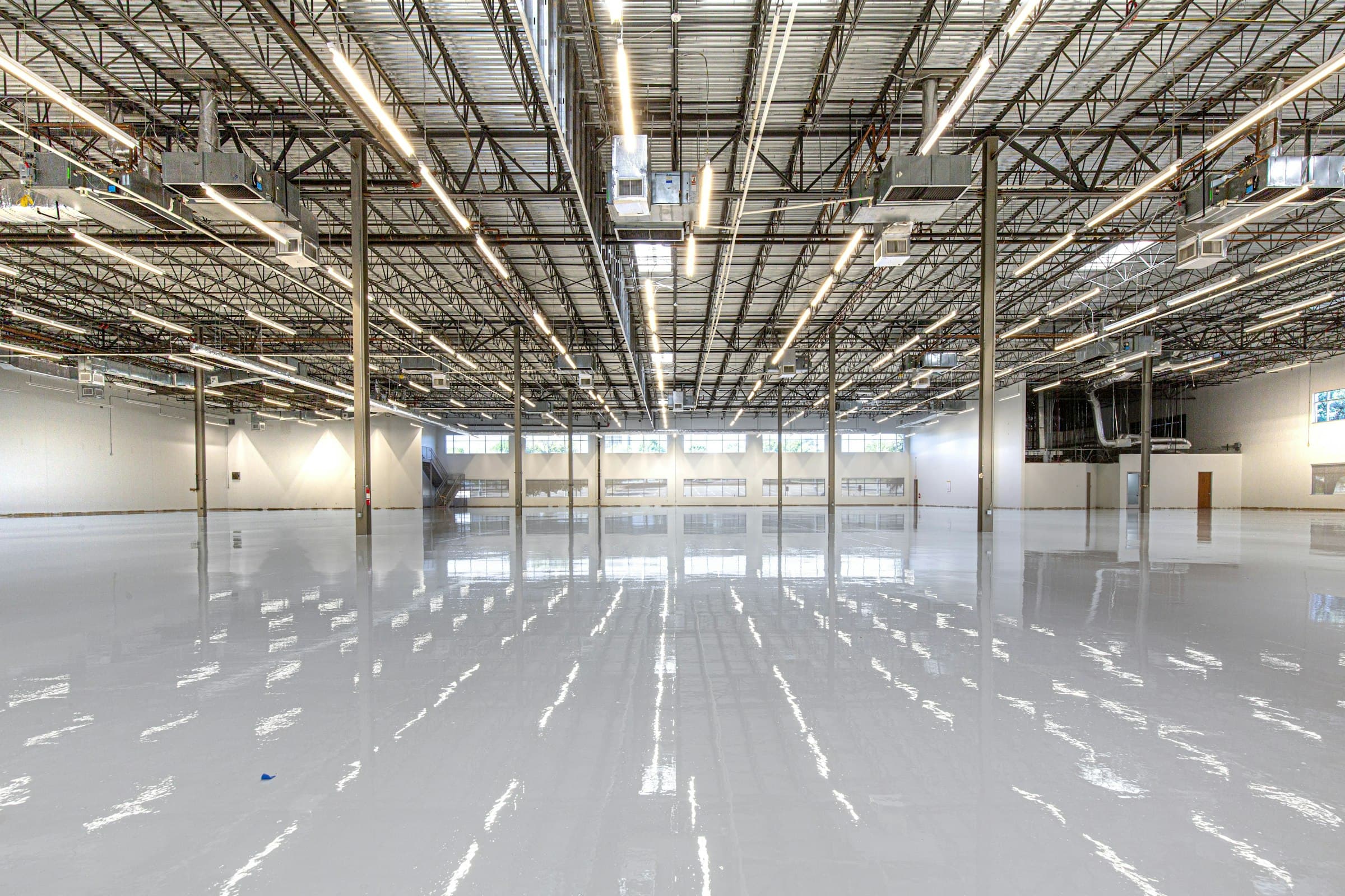 Freshly coated high-gloss epoxy floor reflecting overhead lights in a large open space